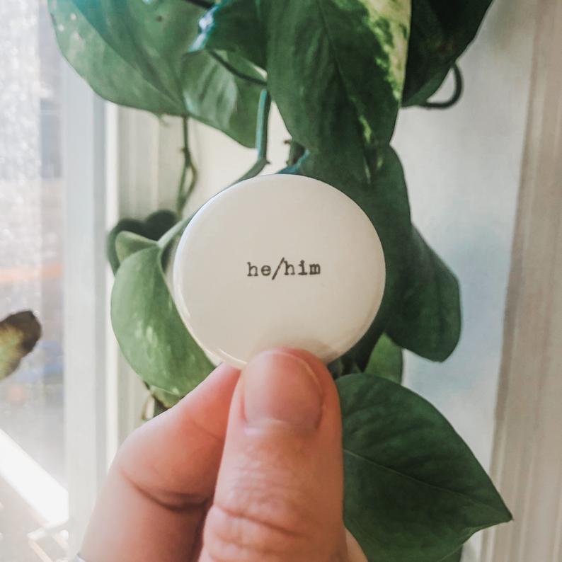 he/him pronouns typed in typewriter font on a white background, 1.5 inch pinback button