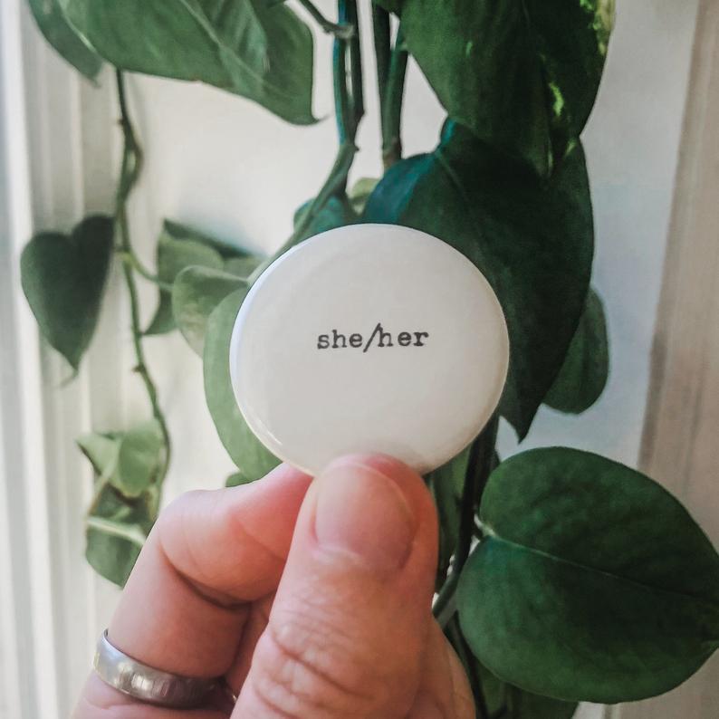 she/her pronouns typed in typewriter font on a white background, 1.5 inch pinback button