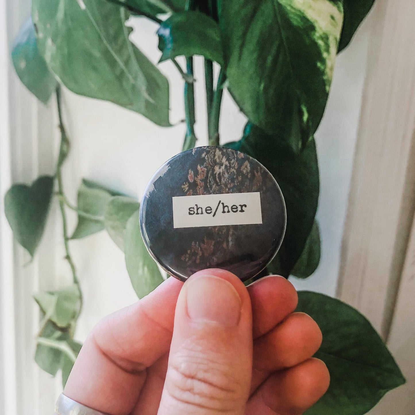 she/her pronouns typed in typewriter font on a colorful background, 1.5 inch pinback button